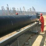 Cold-applied anticorrosion tape being mechanically wrapped around a large-diameter steel pipeline