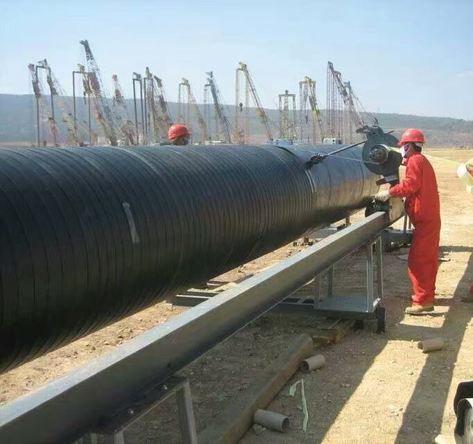 Cold-applied anticorrosion tape being mechanically wrapped around a large-diameter steel pipeline